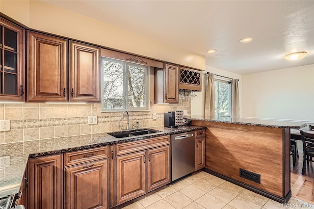 kitchen featuring a peninsula, dishwasher, dark stone countertops, and a sink