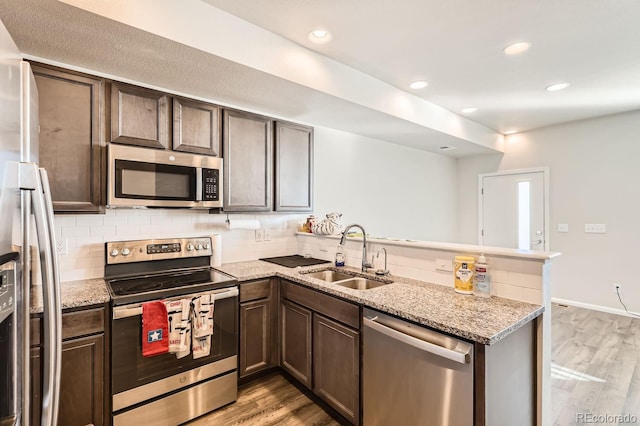 kitchen featuring kitchen peninsula, appliances with stainless steel finishes, light wood-type flooring, light stone counters, and sink