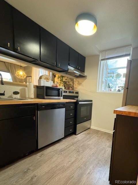 12546 E Cornell Ave Unit 104, Aurora, CO 80014 - kitchen featuring appliances with stainless steel finishes, under cabinet range hood, light wood-style floors, dark cabinetry, and backsplash