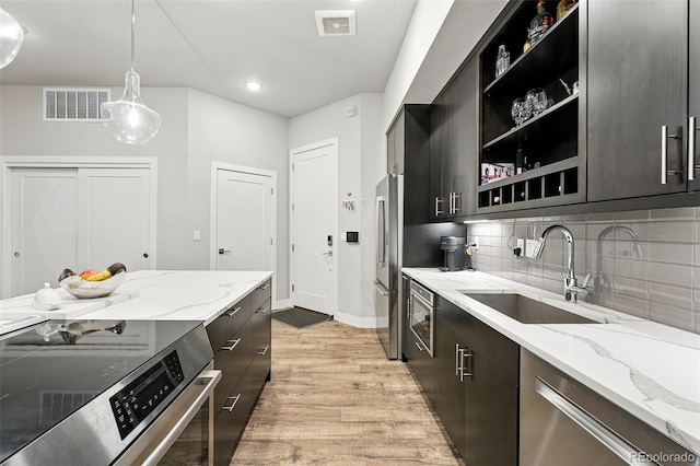 kitchen featuring a sink, appliances with stainless steel finishes, light wood-style flooring, open shelves, and hanging light fixtures