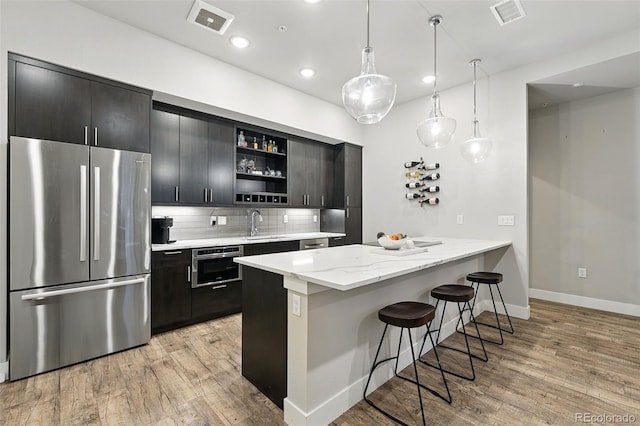 kitchen featuring appliances with stainless steel finishes, open shelves, a kitchen breakfast bar, light wood-style flooring, and baseboards