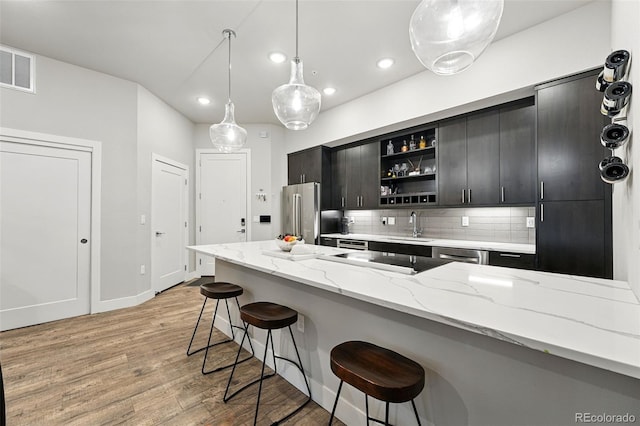 kitchen with appliances with stainless steel finishes, open shelves, a sink, a breakfast bar, and light wood finished floors