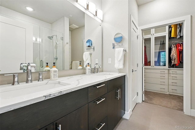 bathroom featuring a shower stall, double vanity, a walk in closet, and baseboards