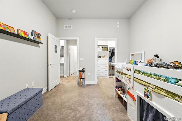 bedroom featuring light colored carpet, a spacious closet, and baseboards