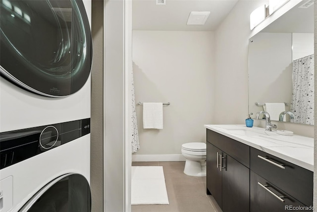 bathroom with stacked washer / dryer, tile patterned floors, toilet, vanity, and baseboards