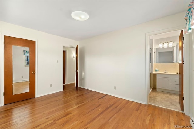 unfurnished bedroom featuring ensuite bath, hardwood / wood-style floors, and a baseboard radiator