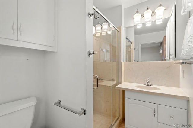 bathroom featuring vanity, toilet, a shower with door, and backsplash