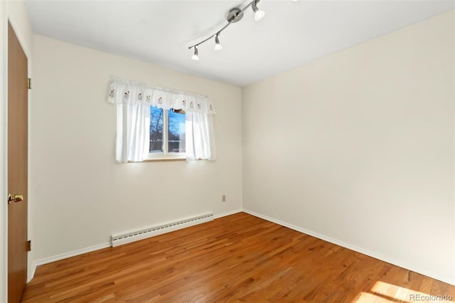 empty room with a baseboard radiator, track lighting, and hardwood / wood-style flooring