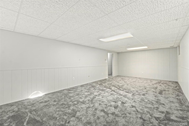 carpeted empty room featuring a drop ceiling and wooden walls