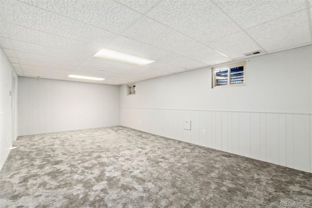 basement with carpet flooring, a paneled ceiling, and wooden walls