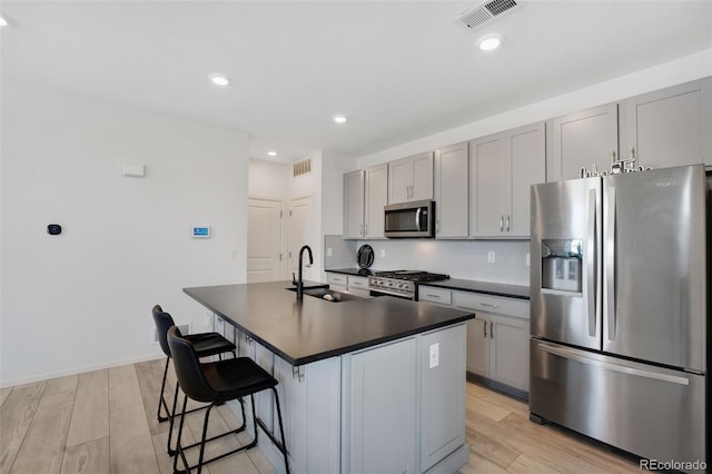 kitchen with an island with sink, sink, gray cabinetry, appliances with stainless steel finishes, and light wood-type flooring