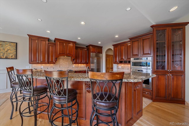 1015 Nob Hill Rd, Evergreen, CO 80439 - kitchen featuring recessed lighting, light wood finished floors, arched walkways, appliances with stainless steel finishes, and custom exhaust hood