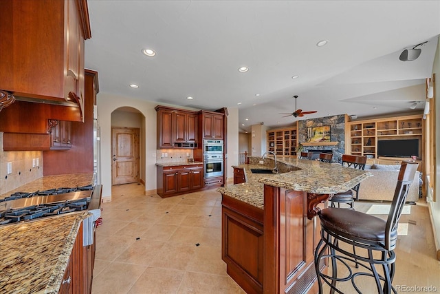 1015 Nob Hill Rd, Evergreen, CO 80439 - kitchen featuring double oven, a ceiling fan, arched walkways, a fireplace, and open floor plan