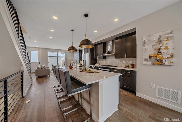 kitchen featuring dark wood-style flooring, light countertops, visible vents, decorative backsplash, and wall chimney range hood