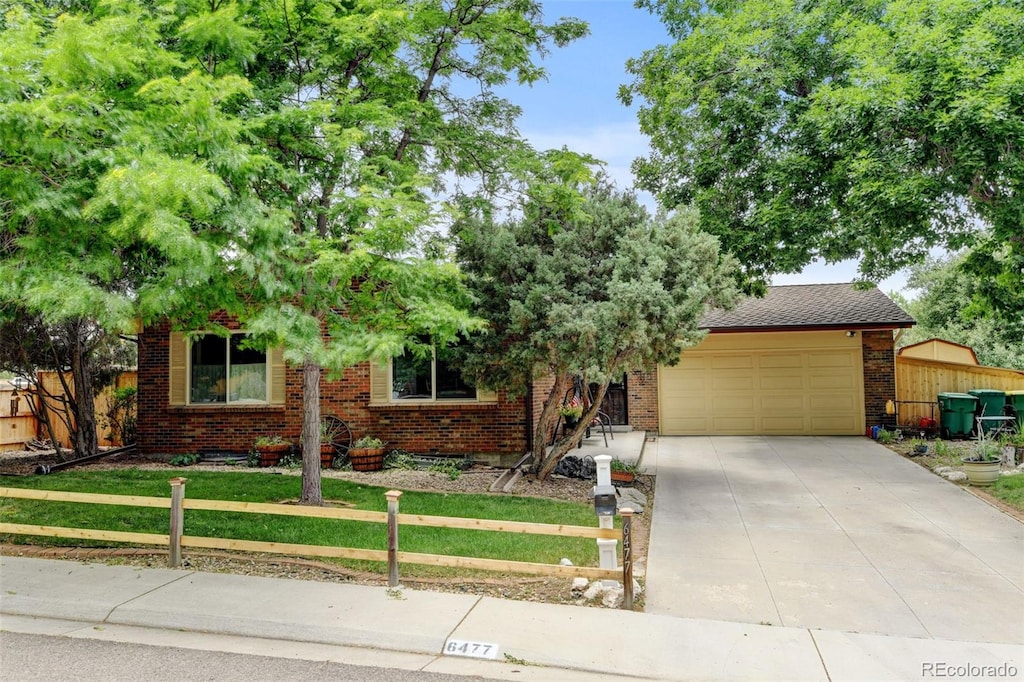 6477 S Brentwood Way, Littleton, CO 80123 - view of property hidden behind natural elements with brick siding, concrete driveway, a garage, and a fenced front yard