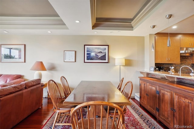 dining area featuring sink, a tray ceiling, dark hardwood / wood-style flooring, and ornamental molding