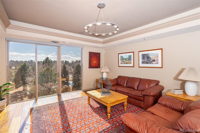 living room with a tray ceiling, wood finished floors, and ornamental molding