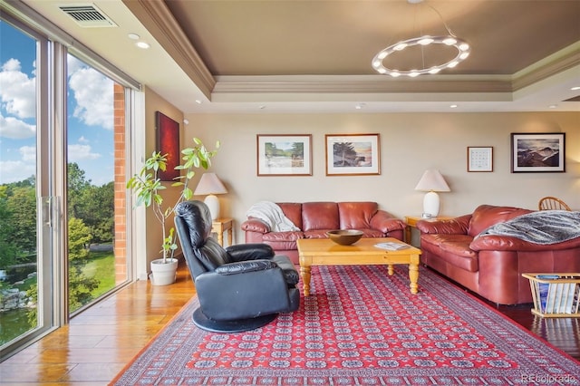 living room with a raised ceiling, wood finished floors, crown molding, and visible vents