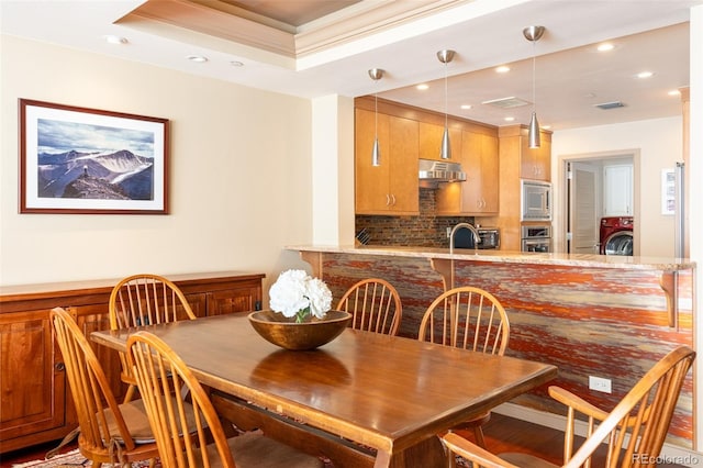 dining room featuring a tray ceiling, ornamental molding, washer / dryer, recessed lighting, and wood finished floors