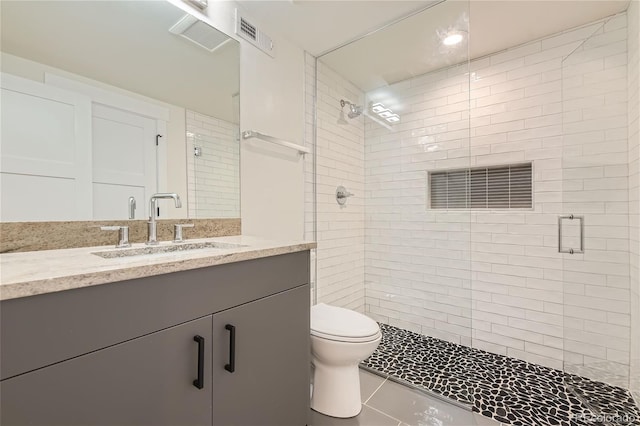 bathroom featuring a tile shower, tile flooring, toilet, and vanity