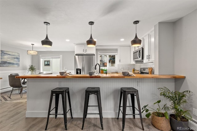 kitchen with a breakfast bar area, white cabinets, light hardwood / wood-style floors, and appliances with stainless steel finishes