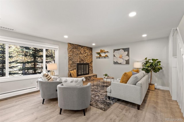 living room featuring light hardwood / wood-style floors, a stone fireplace, and baseboard heating