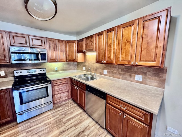 kitchen featuring light wood-type flooring, a sink, appliances with stainless steel finishes, light countertops, and decorative backsplash