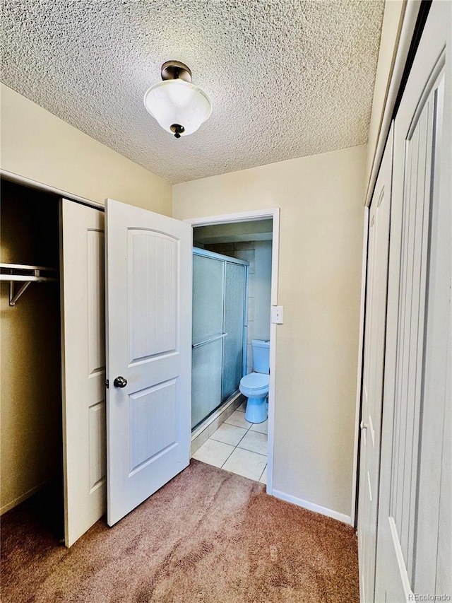 unfurnished bedroom with baseboards, ensuite bath, a closet, a textured ceiling, and light colored carpet