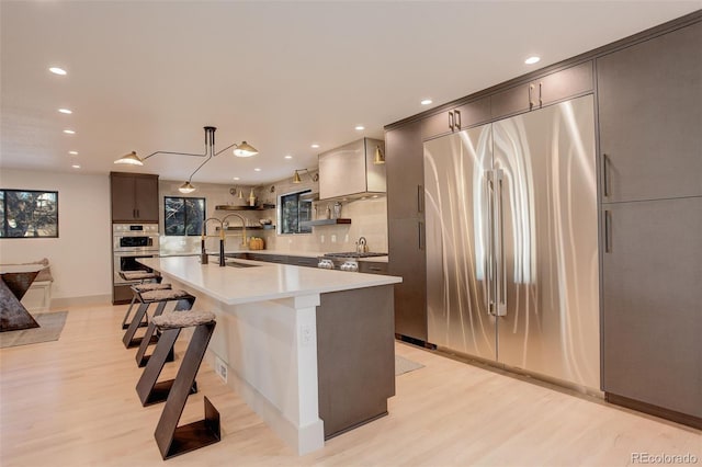 kitchen with sink, a kitchen island with sink, light hardwood / wood-style floors, a breakfast bar area, and stainless steel appliances