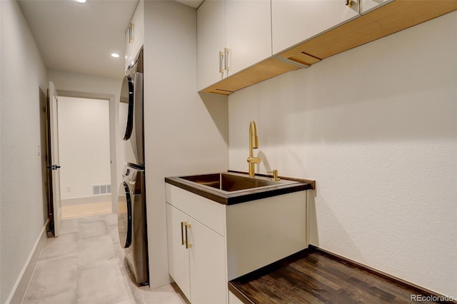 kitchen featuring stacked washer and dryer, white cabinets, and sink