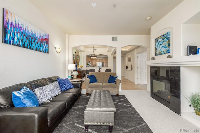 carpeted living room with arched walkways, a tiled fireplace, and visible vents