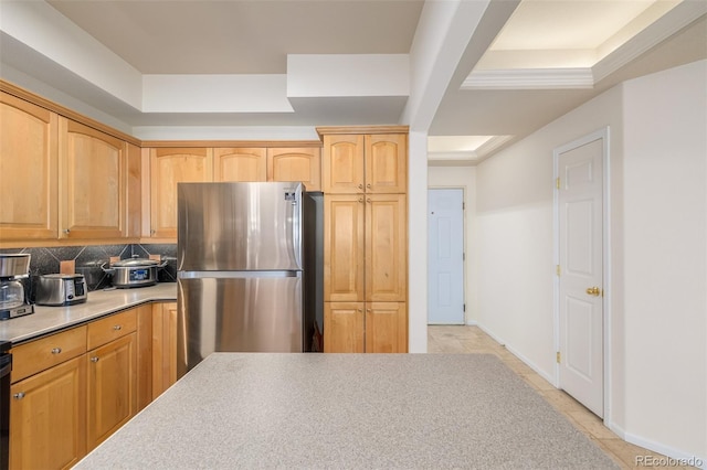 kitchen featuring arched walkways, baseboards, light countertops, freestanding refrigerator, and decorative backsplash