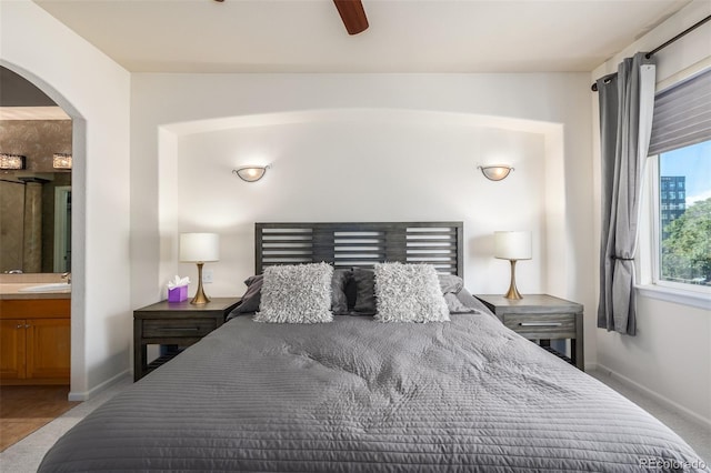 bedroom with arched walkways, connected bathroom, a sink, a ceiling fan, and baseboards