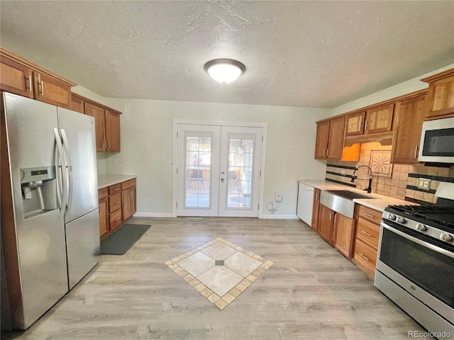 kitchen featuring french doors, light wood-type flooring, backsplash, stainless steel appliances, and sink