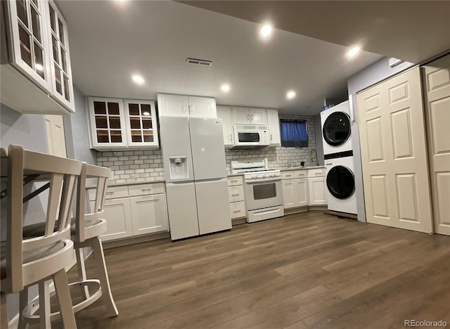 kitchen featuring white cabinetry, dark hardwood / wood-style flooring, backsplash, stacked washer / dryer, and white appliances