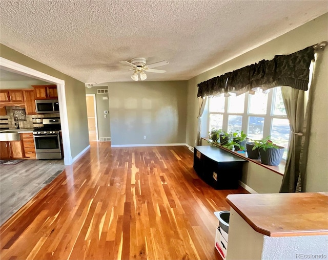 unfurnished living room with ceiling fan, light hardwood / wood-style flooring, and a textured ceiling