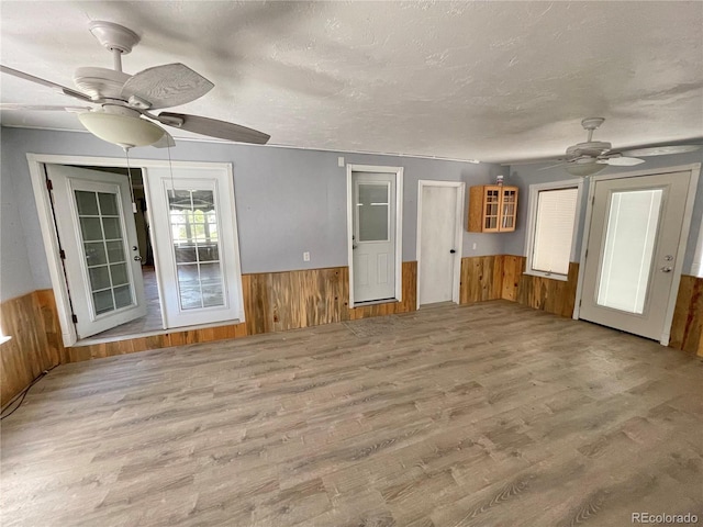 unfurnished living room with light wood-type flooring, a textured ceiling, ceiling fan, and wooden walls