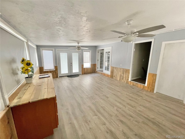 unfurnished living room with wood walls, french doors, light hardwood / wood-style flooring, ceiling fan, and a textured ceiling