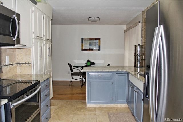 kitchen featuring a peninsula, tasteful backsplash, baseboards, white cabinetry, and appliances with stainless steel finishes