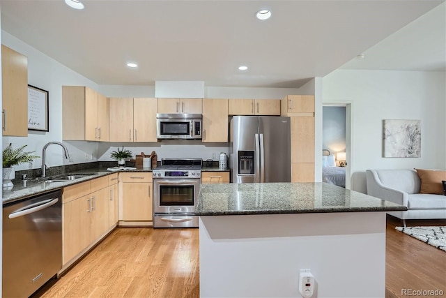 kitchen with appliances with stainless steel finishes, light brown cabinetry, sink, dark stone countertops, and light hardwood / wood-style flooring