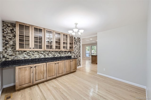 kitchen with light hardwood / wood-style floors, tasteful backsplash, dark stone countertops, an inviting chandelier, and pendant lighting