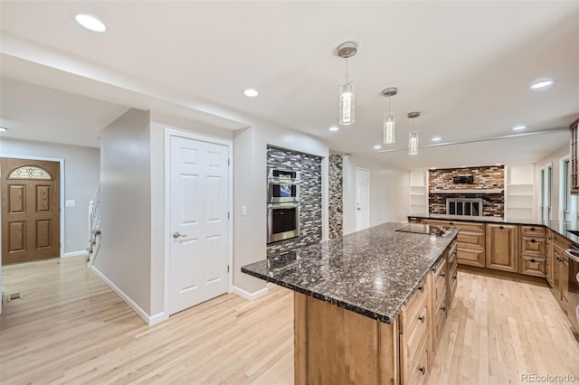 kitchen featuring light hardwood / wood-style floors, dark stone counters, double oven, a fireplace, and decorative light fixtures