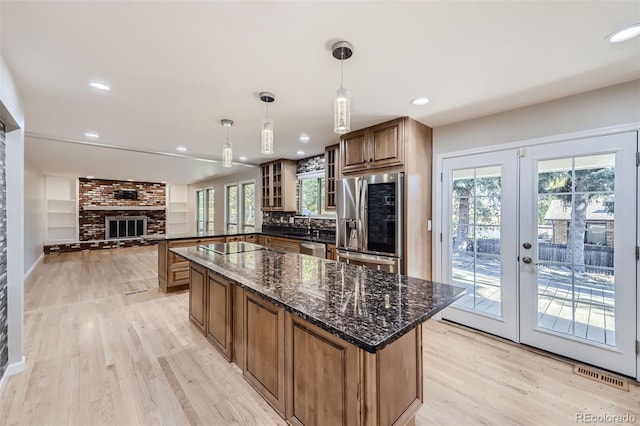 kitchen with french doors, stainless steel appliances, dark stone counters, pendant lighting, and light hardwood / wood-style flooring