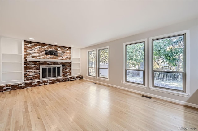 unfurnished living room with built in shelves, light hardwood / wood-style floors, and a brick fireplace