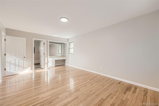 unfurnished bedroom featuring built in desk, connected bathroom, and light hardwood / wood-style flooring