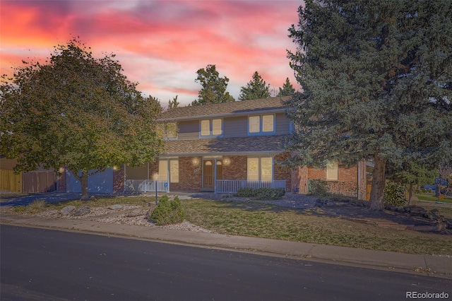 traditional-style home featuring brick siding, covered porch, driveway, and a yard