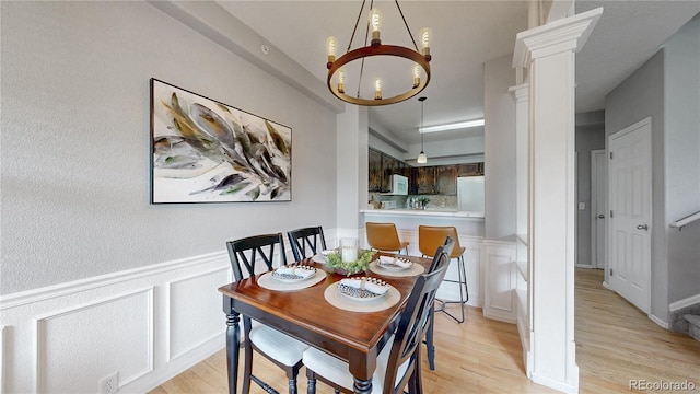 9758 Laredo St Unit 22D, Commerce City, CO 80022 - dining area featuring a chandelier, light wood-style floors, a decorative wall, a wainscoted wall, and ornate columns