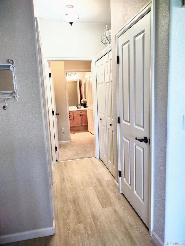 corridor featuring light wood-type flooring, a textured wall, and baseboards