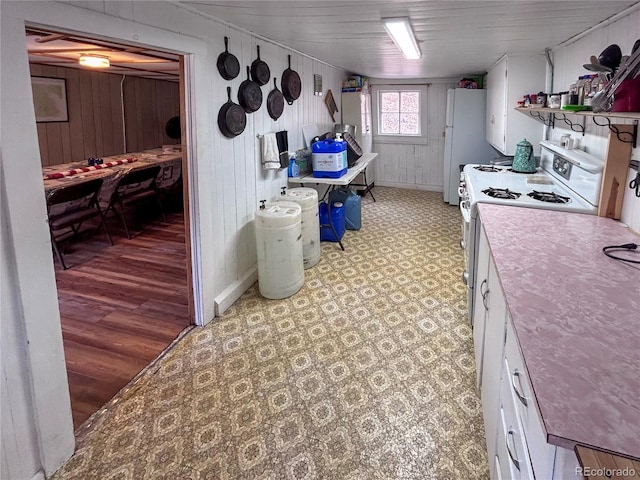 kitchen with wooden walls, white cabinetry, white appliances, and light hardwood / wood-style floors