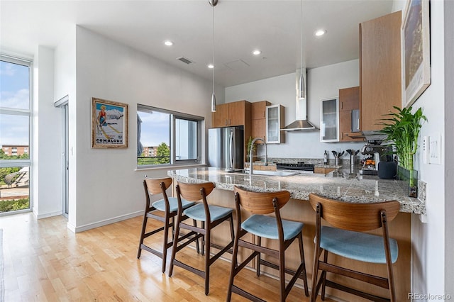 2958 Syracuse St Unit 403, Denver, CO 80238 - kitchen with freestanding refrigerator, brown cabinetry, wall chimney range hood, a peninsula, and glass insert cabinets